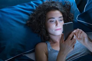 Pretty girl messaging before sleeping at night. Addicted woman suffering from insomnia surfing on the internet with cell.