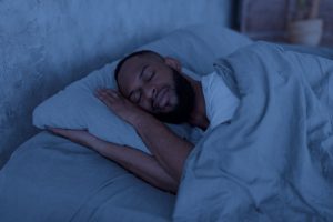 Portrait of happy young well-slept African American man lying in bed with closed eyes