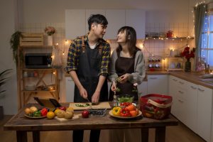 happy asian young couple working together making valentine’s day dinner in a cozy decorated kitchen at home