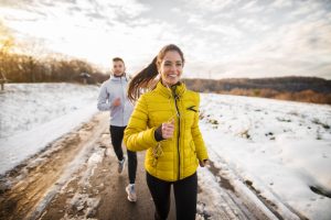 Beautiful happy active couple jogging on a snowy road in nature.