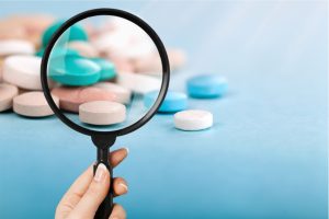 Hand holds up magnifying glass to an assortment of colored pills