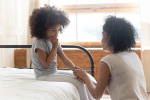 Caring mother talks to her child on bed.