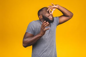 Man in grey t shirt isolated against yellow background smelling something stinky and disgusting.