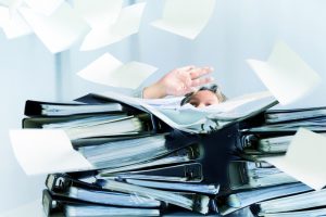 Women behind high stack of black binders feeling overwhlemed with all the work in front of her.