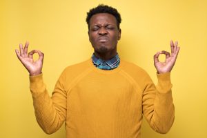 Studio portrait of african young handsome man in meditation pose, trying to relax or calm down in zen