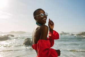 Attractive woman in red dress dancing on the beach with sun glasses on.