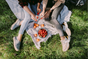 two women sitting at an outdoor picnic eating berries