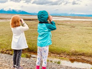 Two children in Alaska use binoculars to look at mountain