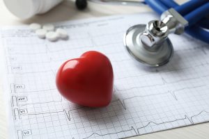 Cardiogram report, red decorative heart, and stethoscope on table.