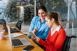 Two women collaborate at a desk with laptops