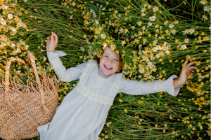 happy cute child in pastel colored dress grins while laying in a patch of wildflowers