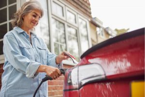 Mature woman charges her electric vehicle outside her home