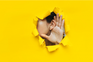 Close-up of a woman's ear and hand through a torn hole in the paper. Yellow background, copy space.