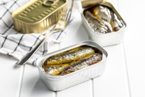 Canned sardines. Sea fish in tin can on white wooden table.