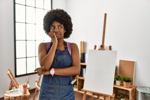 Black woman standing uncertainly in front of an easel and canvas