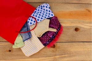 donated clothes spill onto a wooden table top from a red gift bag