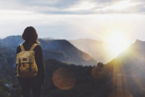 a female traveler's back as she views the sun through a mountainous landscape