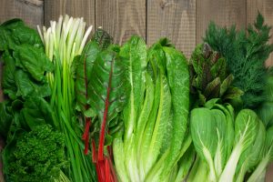 Spring vitamin set of various green leafy vegetables on rustic wooden table.