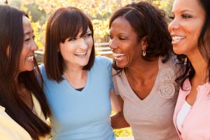 four ethnically diverse adult women smile and laugh with each other