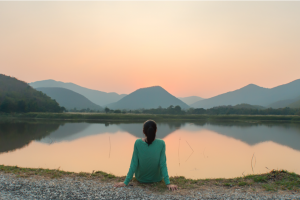 Woman relaxing on the shore of lake during salmon pink sunrise