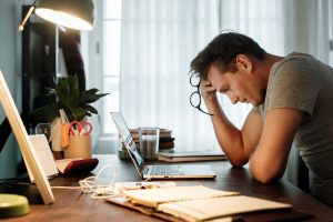 stressed out man hunches over papers while working